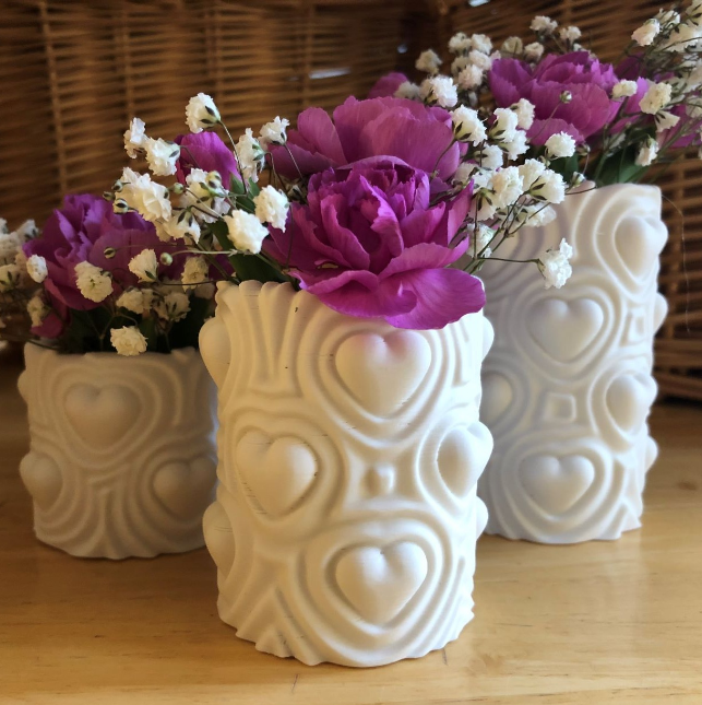 White, 3D-printed Heartbeat Vases with raised heart patterns, filled with purple flowers and white baby's breath. A romantic and stylish thing to 3D print for wife or girlfriend to hold flowers or small bouquets.
