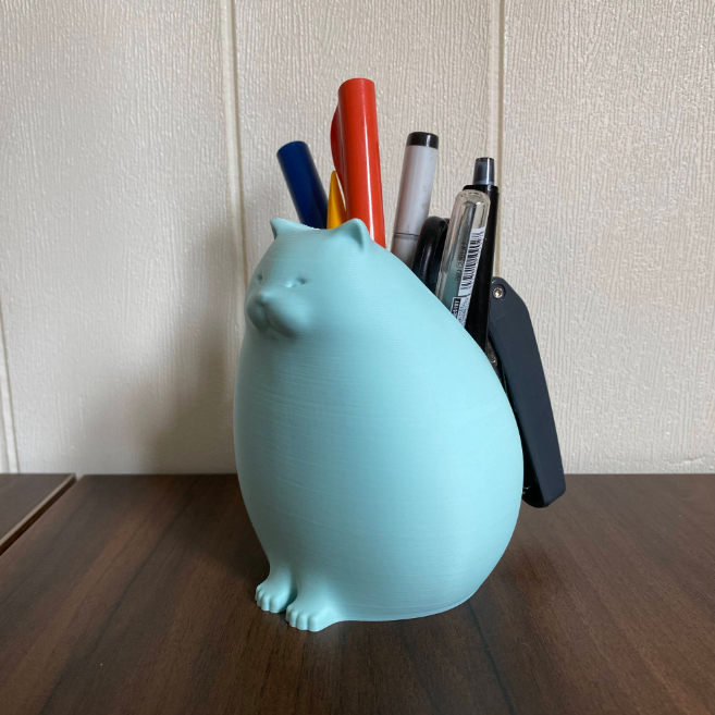 Light blue, 3D-printed cat pencil holder filled with pens and small items. A quirky and functional 3D print idea for wife to organize her stationery on her desk.
