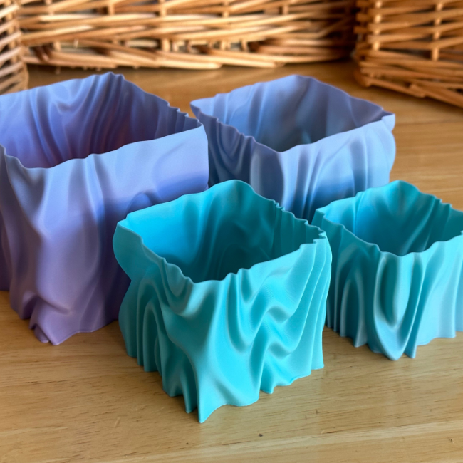 Set of four colorful, wavy 3D-printed Queer Qubes in blue and purple, with a fabric-like texture. Modern and vibrant girly things to make with a 3D printer for storing small items or for decor.
