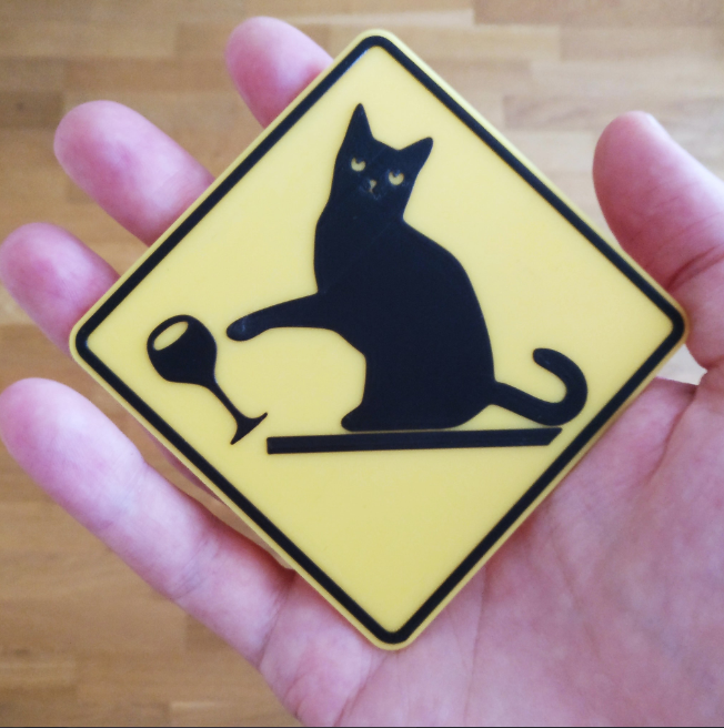 A flat 3D-printed warning sign humorously depicting a cat knocking down objects.
