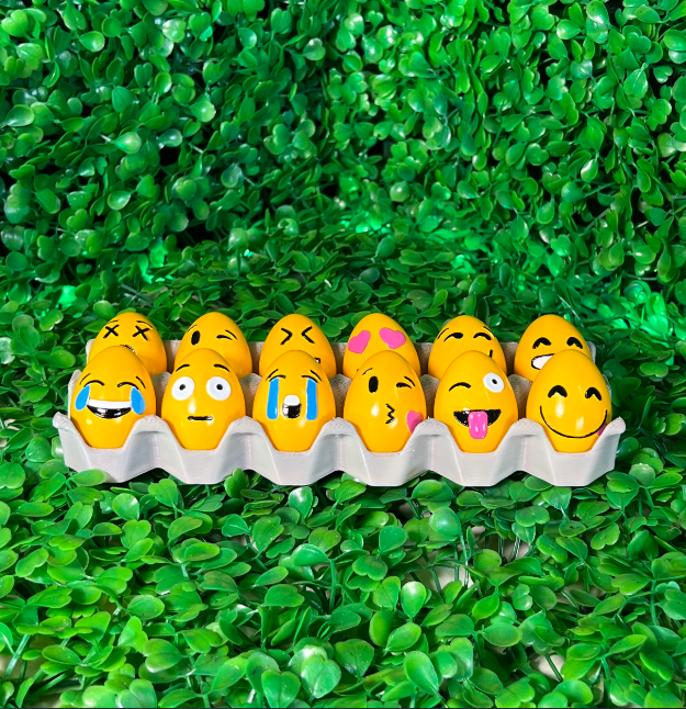 A set of yellow Easter eggs decorated with various emoji faces, sitting on a green background, offering a fun 3D printing project for all ages.