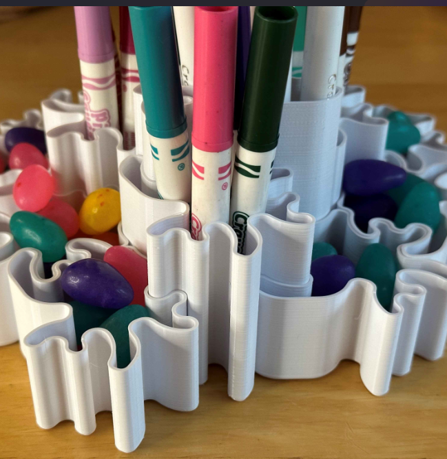 A versatile 3D-printed organizer with flowing, wavy compartments holding colorful markers and jellybeans. This creative design combines functionality and aesthetic appeal, making it ideal for desk or craft space organization.