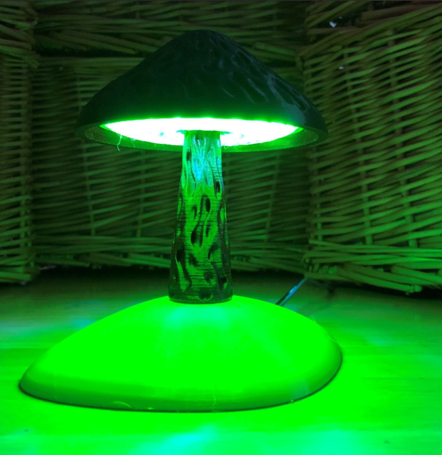 A whimsical 3D-printed mushroom lamp emitting a vibrant green glow, featuring a textured stem and cap design. This unique and playful lighting piece is perfect for adding a touch of fantasy to any room.