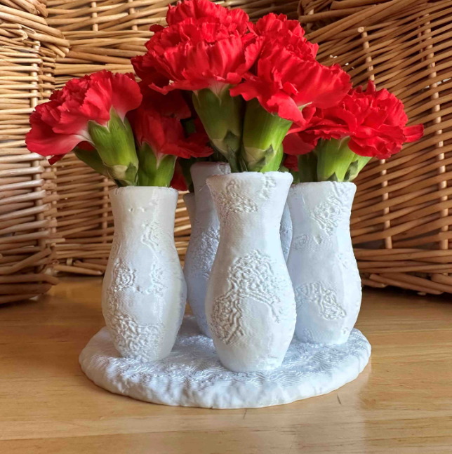 A beautiful 3D-printed multi-vase set holds vibrant red carnations, featuring intricate textured patterns and a shared base. This elegant and functional design is perfect for home decor and a great idea for 'things to 3D print and sell.