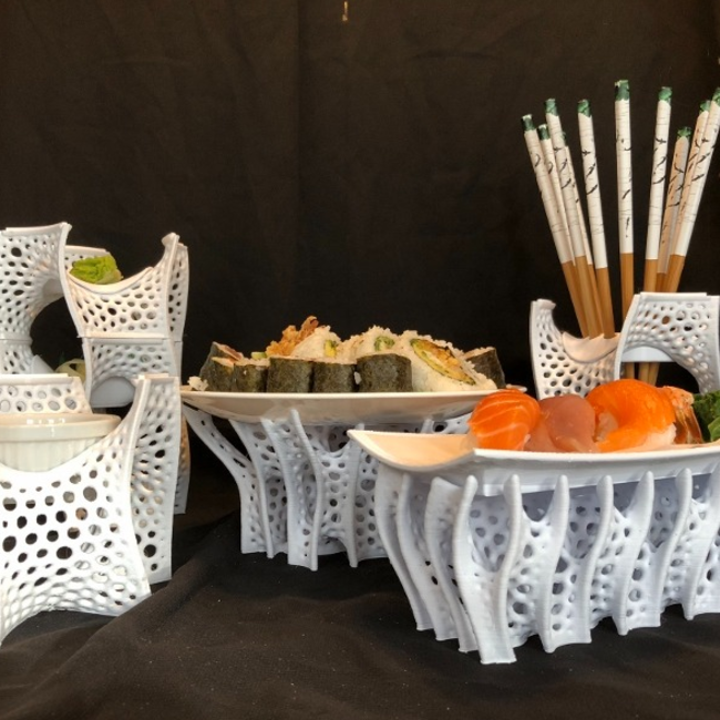 An elegant sushi serving set featuring intricate, 3D-printed white stands with organic, lattice-like designs supporting plates of sushi rolls and sashimi. Chopsticks rest in matching holders, creating a modern and artistic dining presentation.