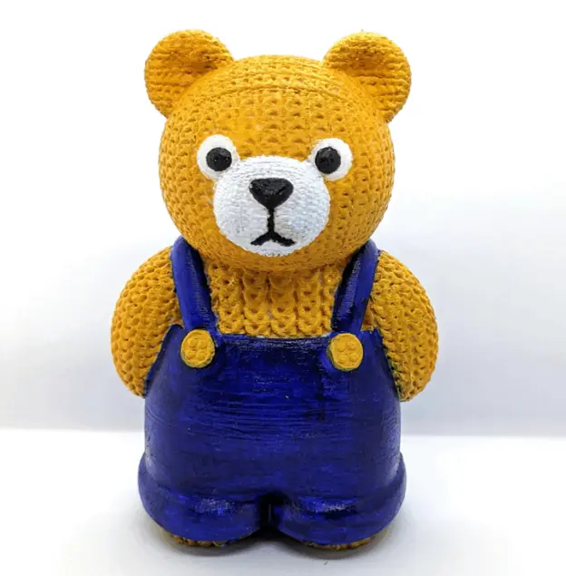一隻黃色熊角色，具有針織紋理，穿著藍色吊帶褲，直立站著。